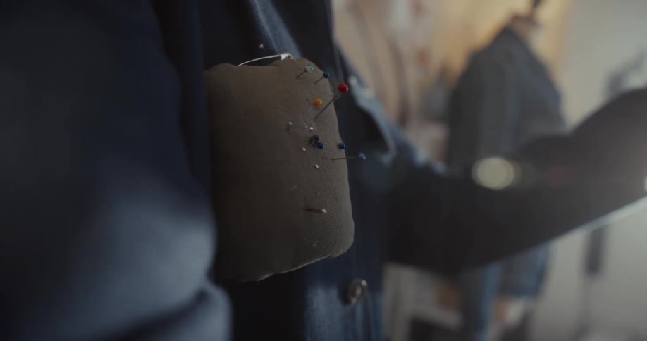 Close up shot of a seamstress pinning colorful needles into a pin cushion on their arm in their studio