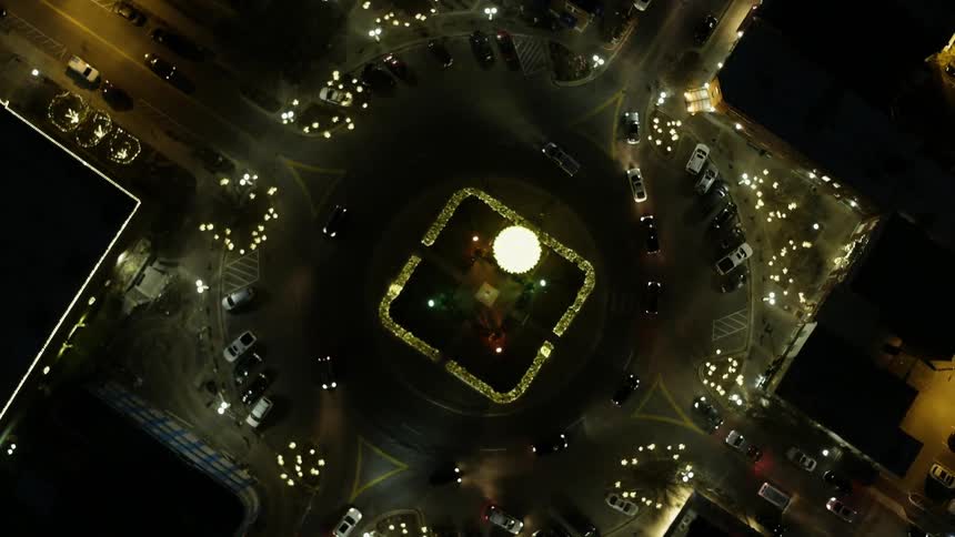 Cars drive around a intersection in a town at night