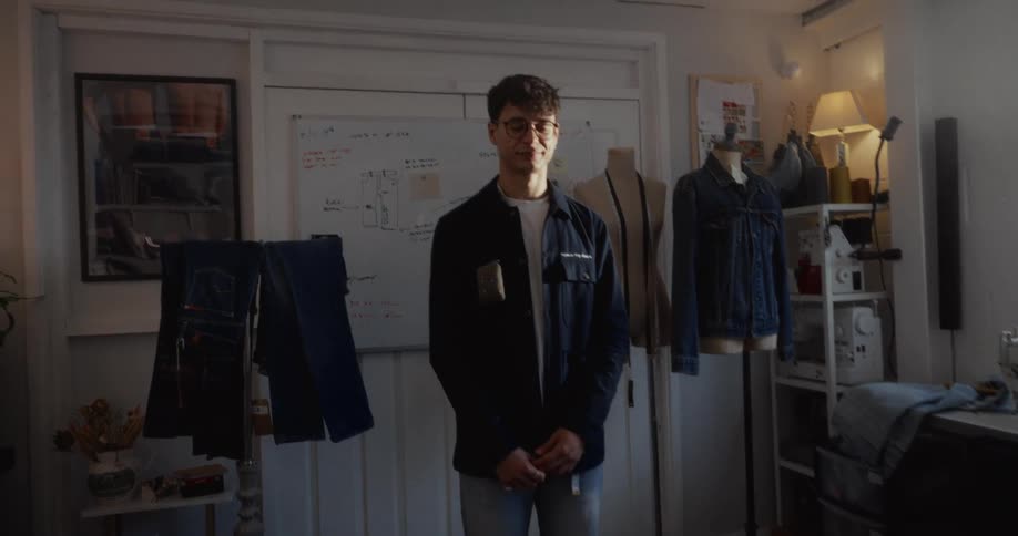A confident young fashion designer smiles for a portrait in his sunlit denim workshop