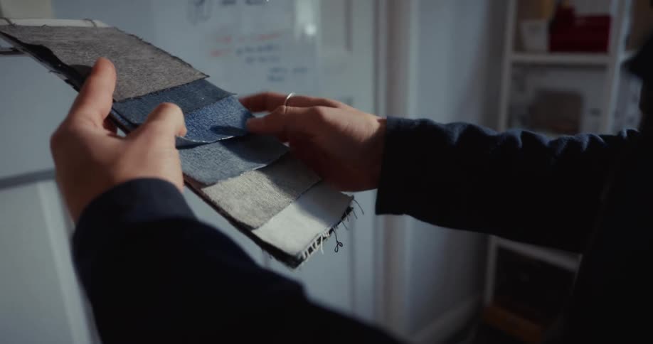 A fashion designer's hands slowly flip through a swatch book of different denim fabric samples