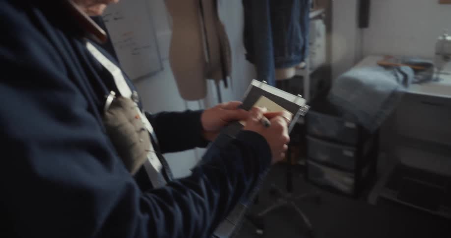 A fashion designer carefully writes notes on a denim fabric swatch book in a creative studio