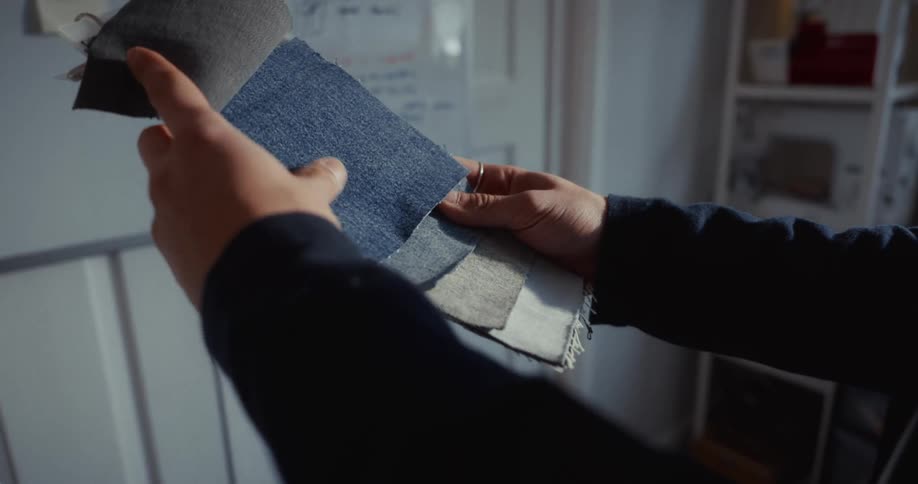 A fashion designer carefully examines a swatch book with different shades of denim fabric in their sunlit studio