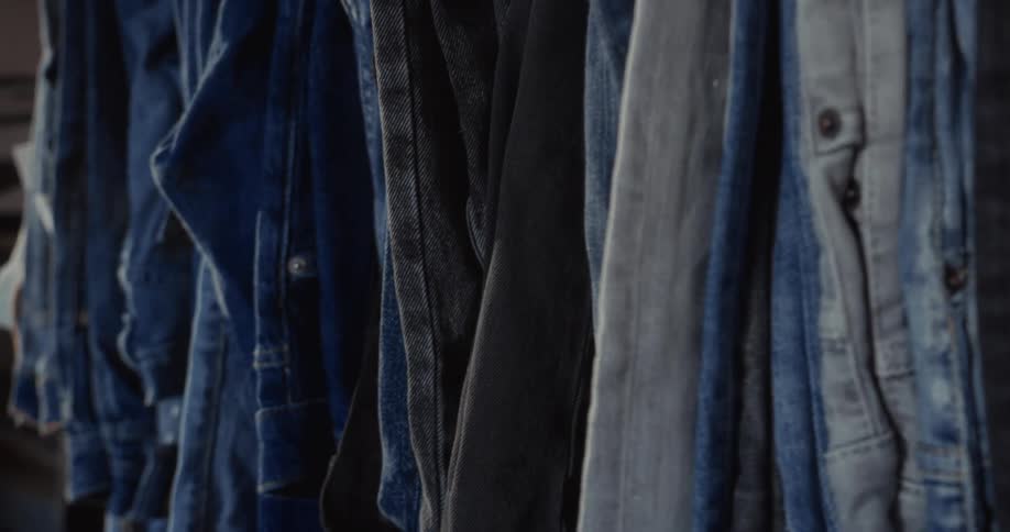 A close-up slow pan of various denim shirts and jackets hanging on a clothing rack