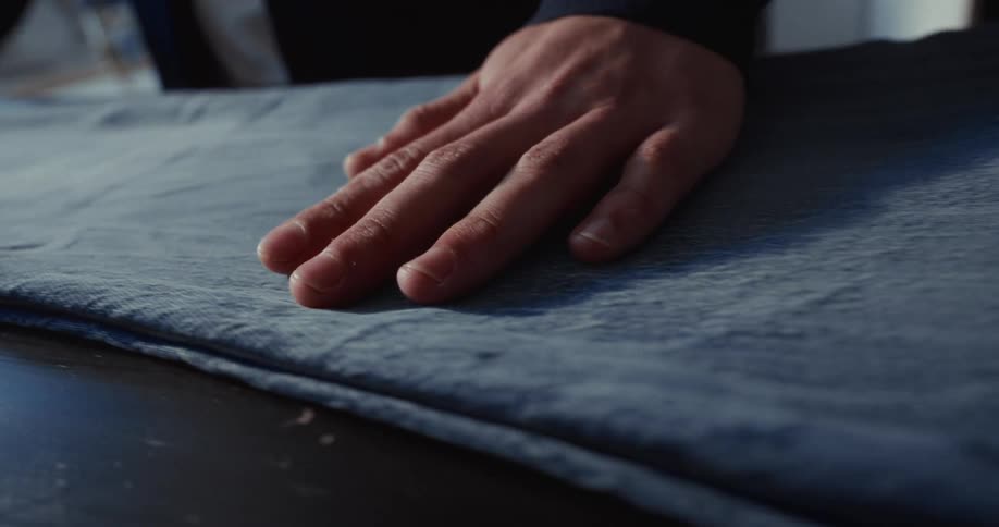 A close-up shot of a hand feeling the texture of a pair of blue jeans on a table