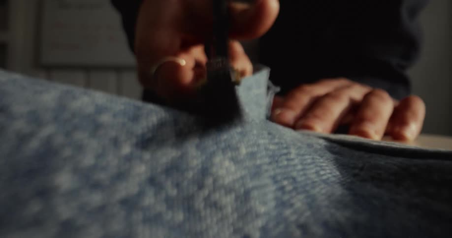 A dynamic, low-angle, extreme close-up of a person's hands cutting blue denim fabric with a pair of scissors