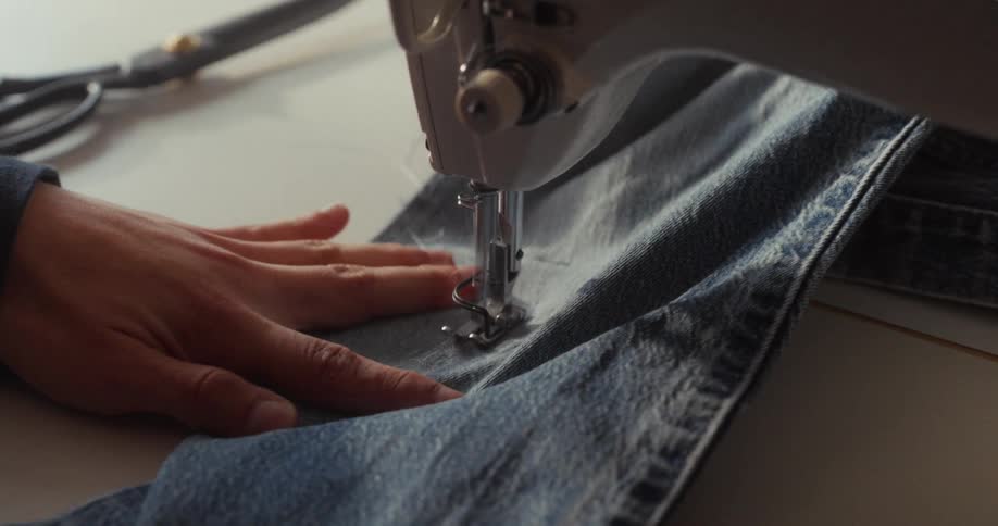 Close-up of a person mending a pair of blue jeans on a sewing machine in slow motion