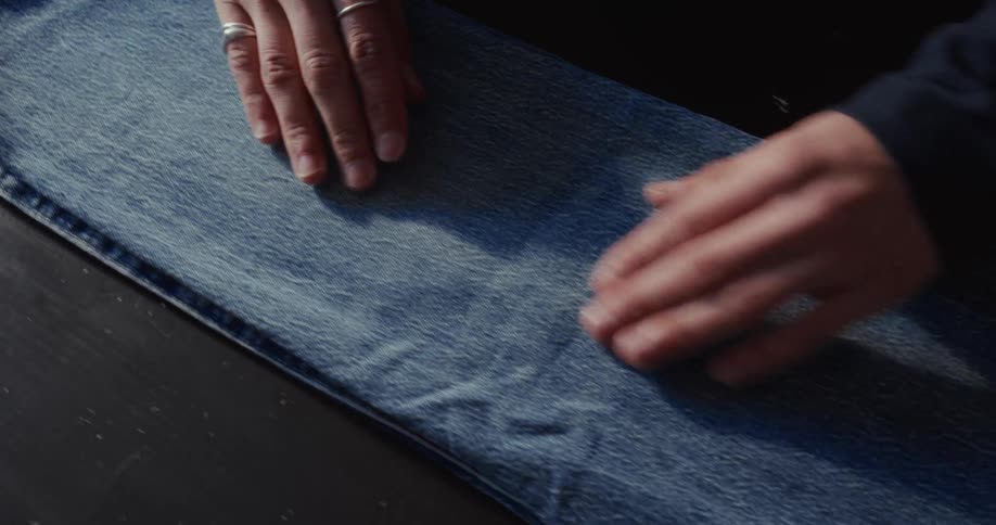 Close-up of a person's hands carefully smoothing out the leg of a pair of blue jeans