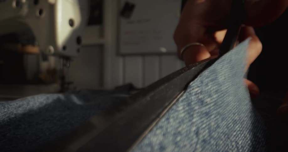 A close-up slow-motion shot of a seamstress cutting blue denim fabric with scissors in a sewing workshop