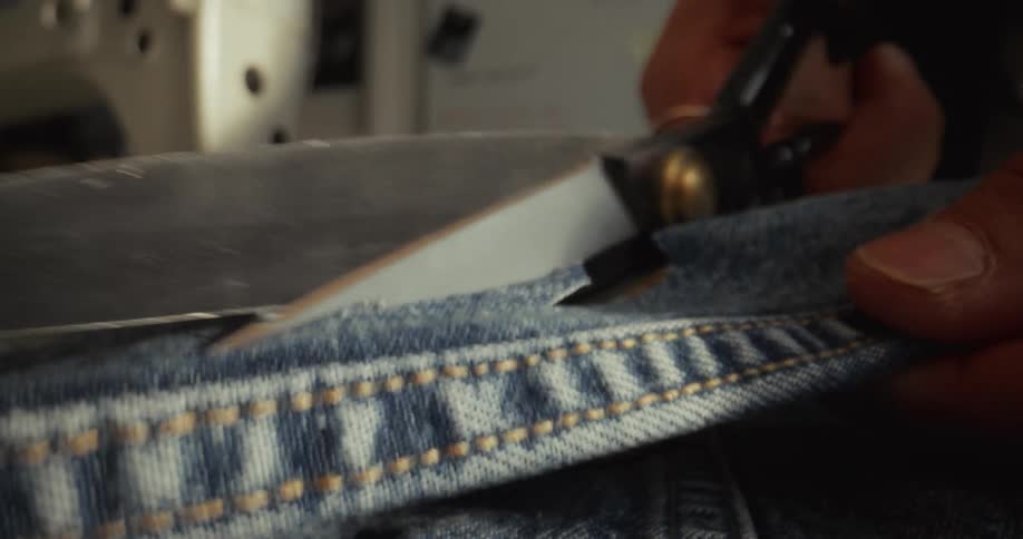 Extreme close-up of scissors cutting through blue denim fabric in slow motion