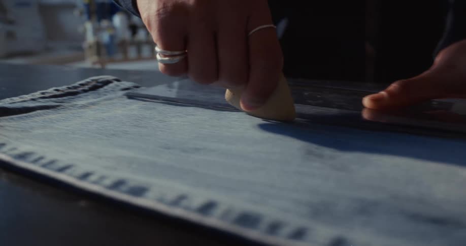 Close up of a tailor's hands using chalk and a ruler to mark a line on a pair of denim jeans in slow motion