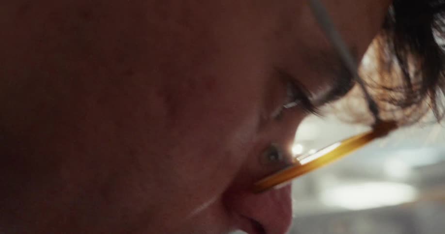 Extreme close-up side profile of a focused individual wearing glasses with a light flare