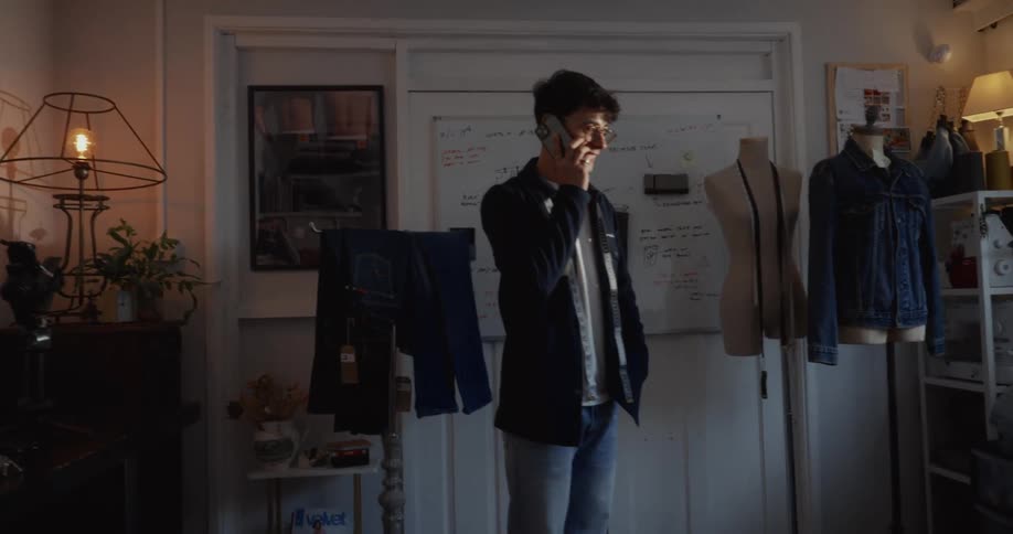 A young male fashion designer talks on the phone while standing in his sunlit design studio