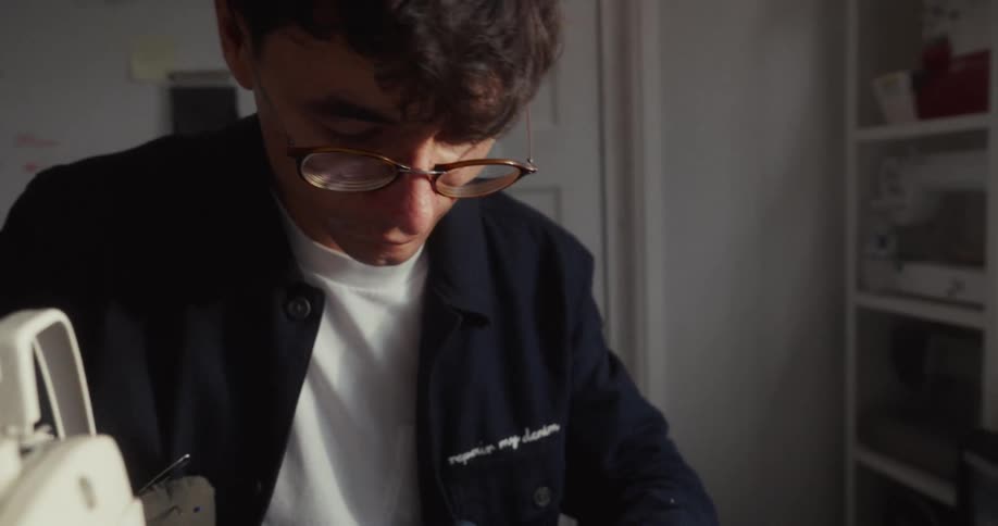 A fashion designer carefully removes stitches from a denim garment with a seam ripper in his studio