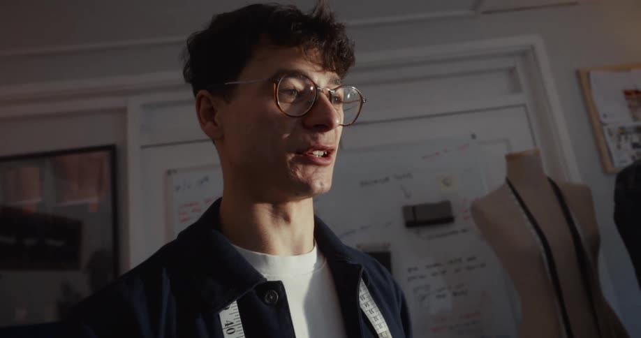 A smiling male fashion designer talks passionately in his sunlit studio as the camera slowly pulls back to reveal his creative workspace