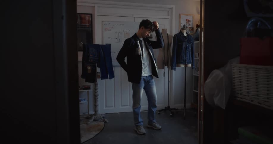 A young clothing designer in his workshop takes a stressful phone call and looks concerned