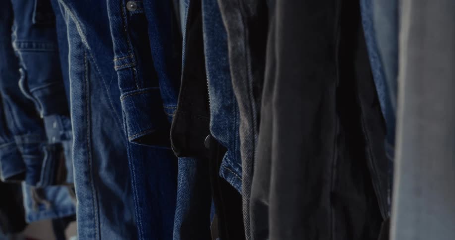 A detailed close-up shot pans across a rack of various blue denim shirts and jackets hanging on wooden hangers