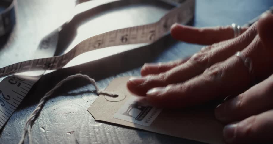 A tailor carefully applies a branded sticker to a paper tag and writes down the order number with a pen