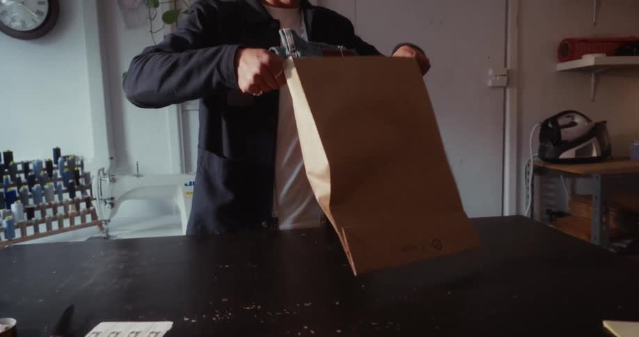 A young tailor in his workshop carefully packages a pair of blue jeans into a brown paper shipping bag