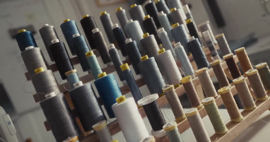 A detailed, slow push-in shot captures a wooden rack filled with colorful spools of thread in a tailor's workshop