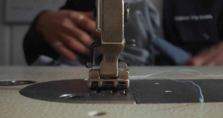 A tailor uses an industrial sewing machine to stitch the hem of a pair of denim jeans