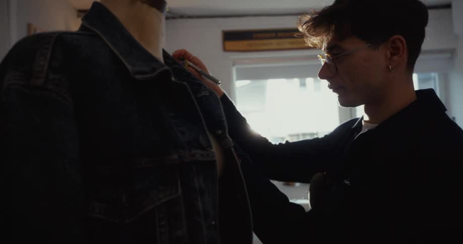 In a sun-drenched studio, a young fashion designer meticulously makes adjustments to a denim jacket on a mannequin