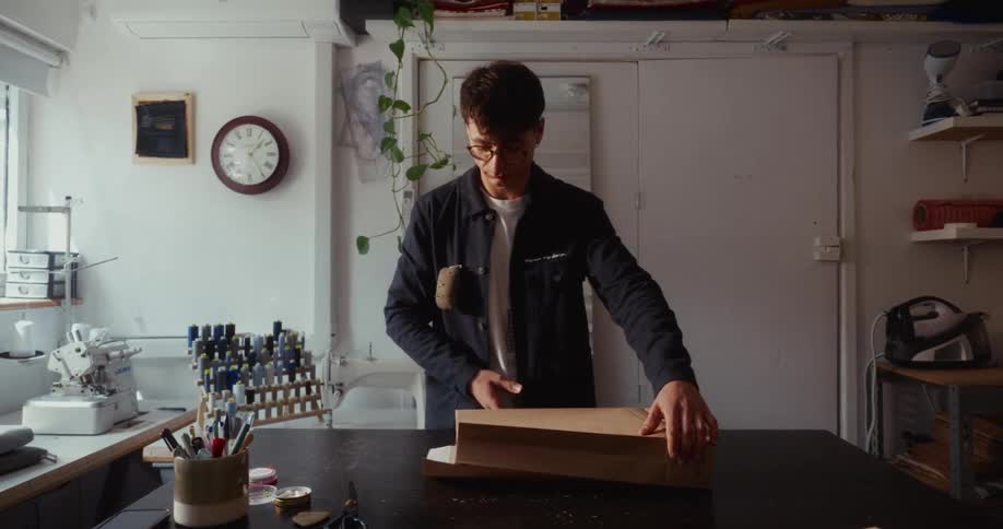 A young fashion designer carefully packages a pair of jeans in sustainable brown paper in his creative workshop