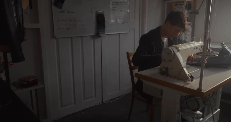 A focused tailor works on an industrial sewing machine in a sunlit studio