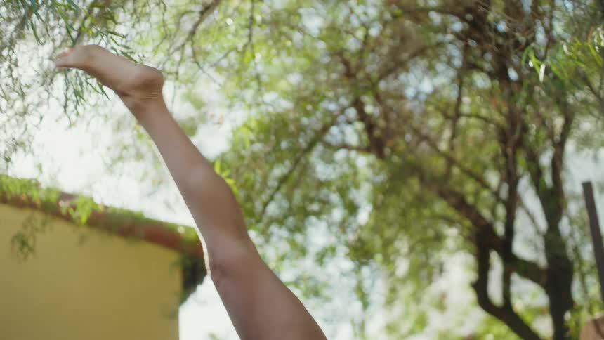 In slow motion, a flexible woman gracefully transitions from a three-legged downward dog to an upward dog pose on a yoga mat in her sunny backyard