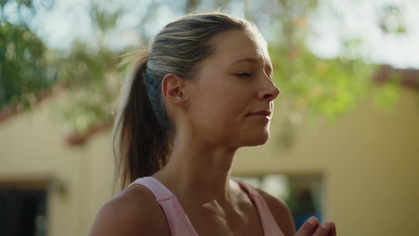 A mindful woman with her eyes closed finds her center while meditating with hands in prayer pose outdoors