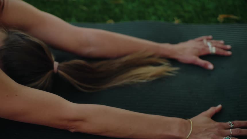 A woman in a pink top holds a peaceful Child's Pose on a yoga mat while practicing outdoors on the grass