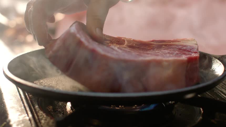A raw steak is put in a smoking frying pan