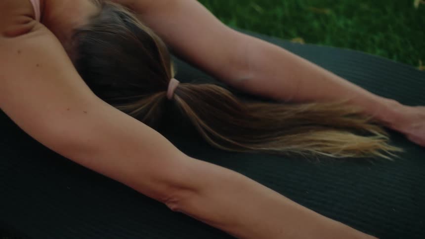 A slow pan reveals a woman stretching into the Child's Pose on her yoga mat placed on lush green grass