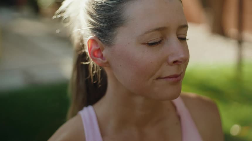 Close-up of a serene woman with her eyes closed, peacefully meditating in a sunlit backyard