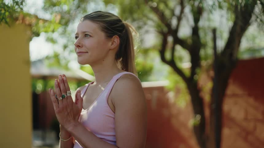 A peaceful woman holds a steady tree pose with her hands in prayer, practicing yoga and mindfulness outdoors in a sunlit garden