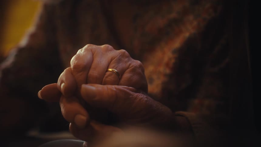Elderly married couple holds hands in a loving embrace, close-up shot on their wrinkled hands and wedding ring