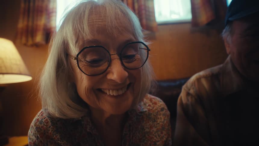 A happy elderly couple smiles and reminisces while looking through an old photo album together in their living room