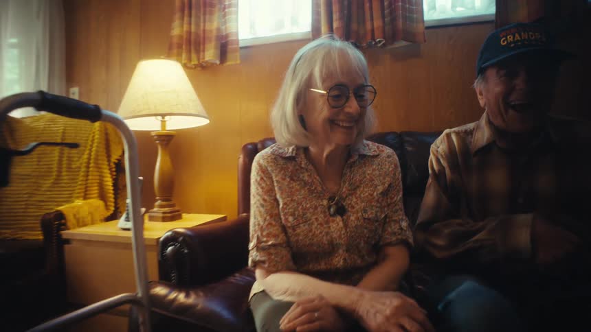 A slow push-in shot captures a happy elderly couple laughing together as they look through a photo album and reminisce in their living room
