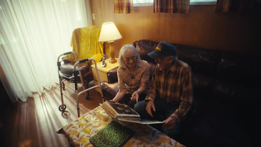 A loving elderly couple share a moment of nostalgia while looking at a photo album in their sunlit living room