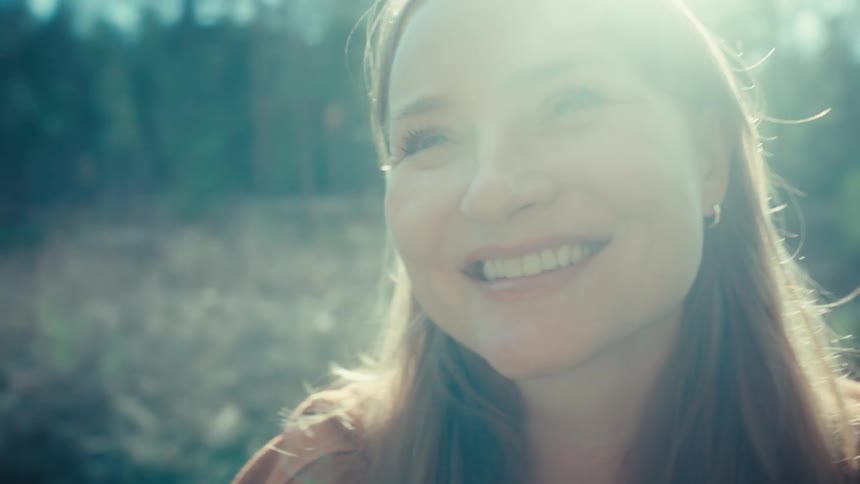 A happy woman smiles while basking in the warm, bright sunlight in a peaceful forest