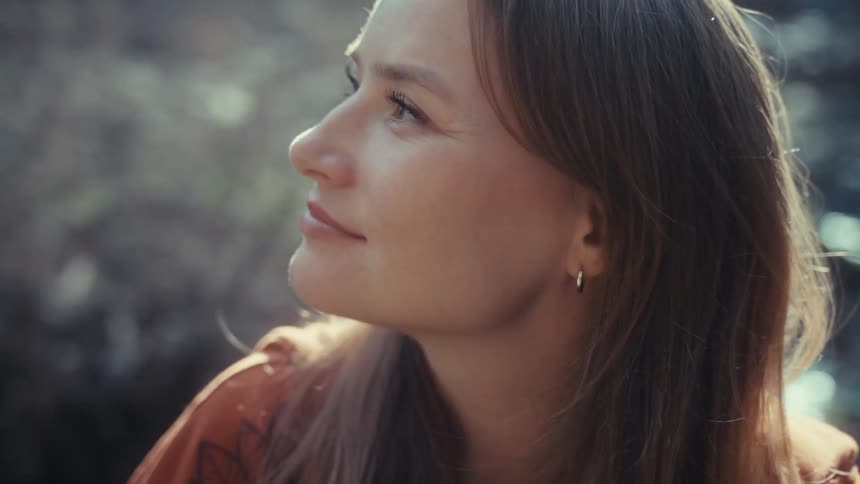 A thoughtful woman enjoys a peaceful moment in nature, looking up with a soft, contented smile