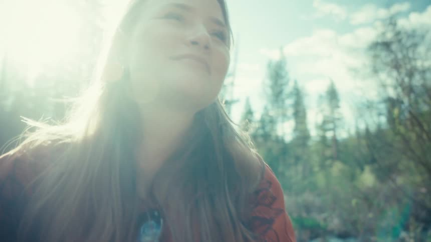 A serene young woman basks in the bright sunshine, smiling peacefully while surrounded by a tranquil forest