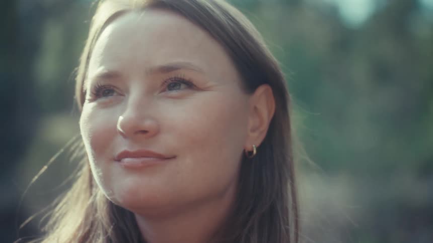 A serene woman smiles peacefully while enjoying the warm sunlight in a tranquil forest setting