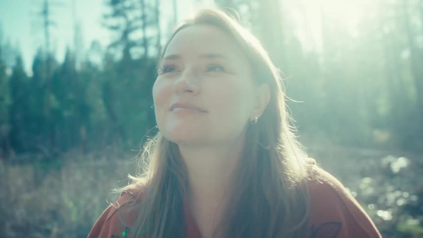A peaceful woman closes her eyes and smiles as she soaks in the warm sunlight in a tranquil forest setting