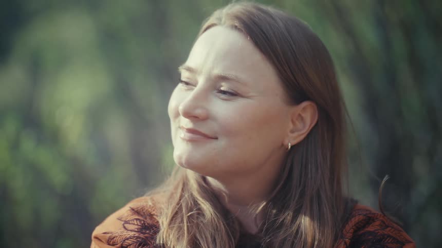 A beautiful woman with a gentle smile enjoys a tranquil moment in nature, basking in the sunlight