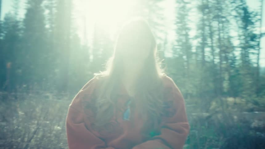 A smiling woman sits on a log and soaks in the warm sunshine in a tranquil forest