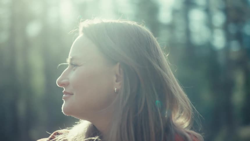 A woman's face glows as she smiles contentedly, enjoying a peaceful, sunny day in the forest