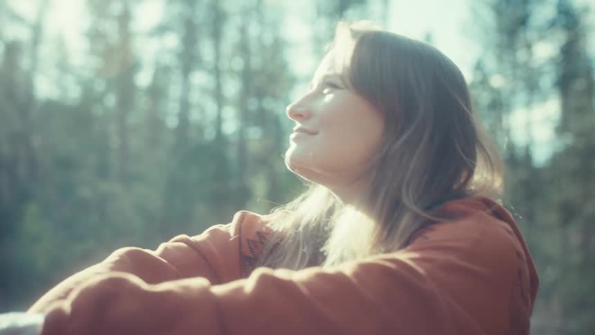 Profile of a smiling young woman basking in the bright, warm sunlight of a peaceful forest