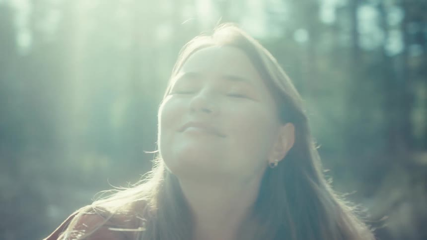 A serene woman soaks in the warm sunlight while sitting peacefully on a log in a beautiful, hazy forest