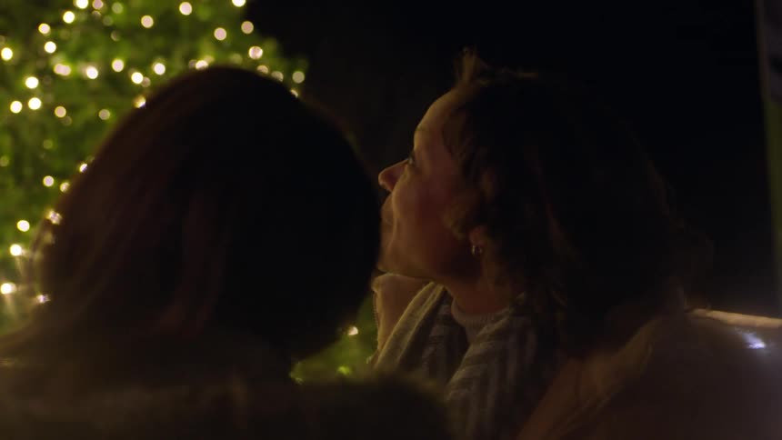 Two women look up at a lit christmas tree at night