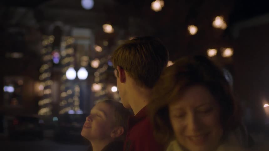 A family looks at christmas decorations on a city sidewalk at night